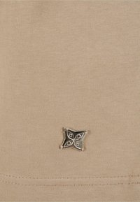 Beige színű pamut szövet, sima textúrával, az alján fémes ezüst csillag alakú díszítéssel, varrott részletekkel.