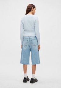 Ανοιχτό μπλε πλεκτό πουλόβερ με ριμπ τελείωμα, συνδυασμένο με ελαφρώς ξεβαμμένα τζιν culottes με ξέφτια στα άκρα. Φορεμένο με μαύρα chunky παπούτσια και λευκές κάλτσες.