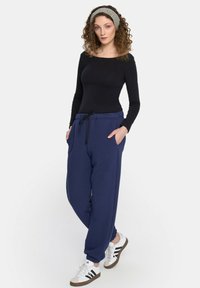 Granatowe dresy z elastycznym pasem i sznurkiem, bocznymi kieszeniami oraz ściągaczami, w połączeniu z czarną bluzą z długim rękawem i białymi trampkami.