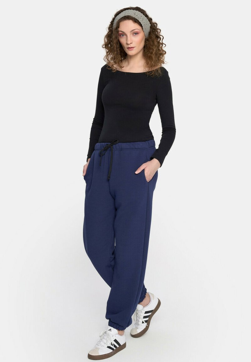 Granatowe dresy z elastycznym pasem i sznurkiem, bocznymi kieszeniami oraz ściągaczami, w połączeniu z czarną bluzą z długim rękawem i białymi trampkami.