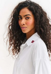 Biała koszula na guziki o luźnym kroju, z bordo akcentem na kołnierzyku, gładką tkaniną i miękką fakturą.