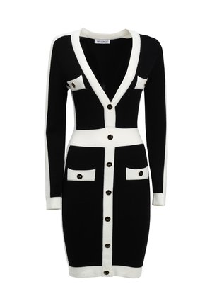 Abito lavorato a maglia in bianco e nero, con maniche lunghe, scollo a V, tasche a contrasto, grandi bottoni neri e una silhouette aderente.