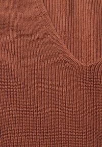 Rostfarbener gerippter Stoff mit einer strukturierten Oberfläche, der vertikale Linien und einen V-Ausschnitt aufweist. Weiches und elastisches Material.