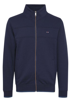 Tumeshi vetline kraavi krae, tekstuurse pind, kontrastne lukustus ja küljetaskud. Rinna kohal väike logo.