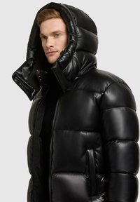 Black puffer jacket with a glossy finish, a large hood, zip closure, and side pockets. Features quilted sections for insulation.