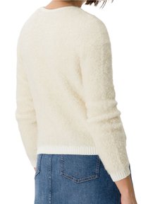 Hellbeige, flauschiger Pullover mit rundem Halsausschnitt und geripptem Saum. Lange Ärmel mit strukturiertem Finish. Kombiniert mit einem Jeansrock.
