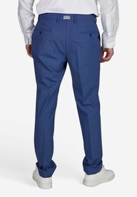 Blaue gemusterte Hose aus leichtem Stoff, mit tailliertem Schnitt, seitlichen Taschen und knöpfbaren Gesäßtaschen, kombiniert mit weißen Sneakers.