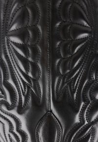 Černá kožená bota s texturovanými, raženými vzory a dekorativním prošitím. Design obsahuje plynulé tvary a detailní akcenty.