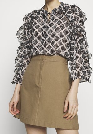 Chemisier imprimé avec des manches volantées, arborant un motif en diamants noir et blanc, associé à une jupe beige taille haute.