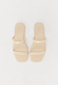 Beige slidesandaler med en glat, blank finish. Har en bred rem over tæerne og en tyndere ankelrem. Flad såldesign.