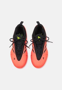 Fényes korall és fekete sportcipők letisztult dizájnnal, sima szintetikus anyagból, texturált fűzőkkel és fényvisszaverő kiegészítőkkel rendelkeznek.