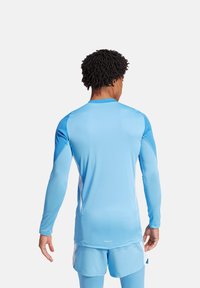 Maglietta sportiva a maniche lunghe di un blu chiaro con pannelli strutturati sulle spalle e un design aderente. Abbinata a pantaloni corti coordinati per un look sportivo.