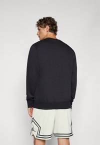 Sort sweatshirt med lange ærmer, rund halsudskæring og ribbede manchetter. Kombination med lyse, mønstrede netshorts. Enkel og funktionel design.