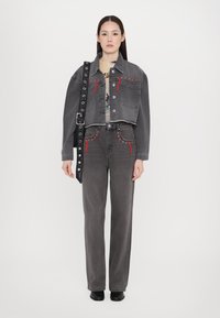 Cropped gray denim jacket with red stitching details, high-waisted gray jeans with similar accents, and a black studded strap bag.