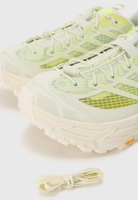 Baskets de trail running vert clair avec une tige en maille texturée, des accents réfléchissants et une épaisse semelle blanche. Comprend un lacet jaune.