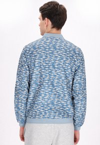 Blue bomber jacket featuring a white fish pattern, ribbed cuffs and hem, smooth texture, and relaxed fit.
