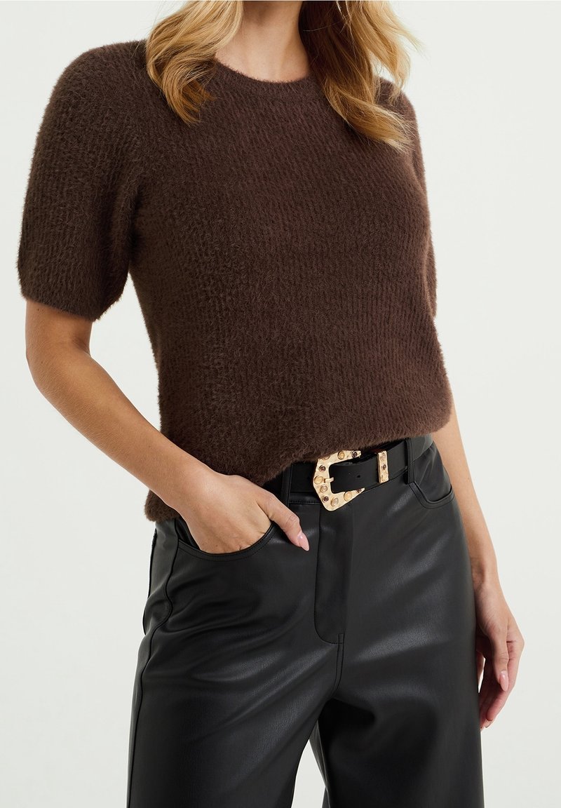 Brun kortärmad stickad tröja med en texturerad yta, matchad med höga svarta läderbyxor och ett kontrasterande spännbälte.