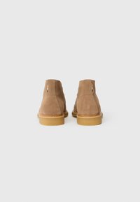Botine din suede, de culoare bej, cu un finisaj texturat, vârfuri rotunde și tălpi din cauciuc. Prezintă două accente de cusătură verticală în spate.