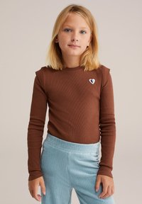 Top marrón de manga larga con textura acanalada y acentos en los hombros, que presenta un pequeño bordado de un corazón azul, combinado con pantalones acanalados de color azul claro.