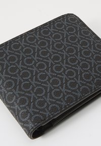 Portofel negru din material texturat, cu un model peste tot format din litere interconectate de culoare albastră. Marginile sunt rotunjite; designul este compact.