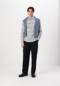 Pulover albastru deschis așezat peste o cămașă cu flori cu butoni. Pantaloni negri, croiți, și pantofi negri completează ținuta. Design simplu, modern.