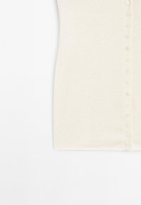 Tissu tricoté de couleur crème avec une rangée verticale de petits boutons assortis le long du bord droit.