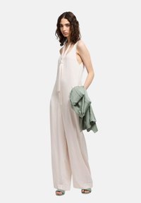 Mono sin mangas de color rosa pálido con un detalle de nudo en el escote; acompañado de una chaqueta verde clara. Tejido suave, piernas anchas y lados abiertos.