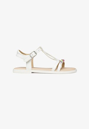 Sandalia plana blanca con correa al tobillo, hebilla plateada, dos finas correas para los dedos y decoración de cuentas multicolores en la correa frontal.