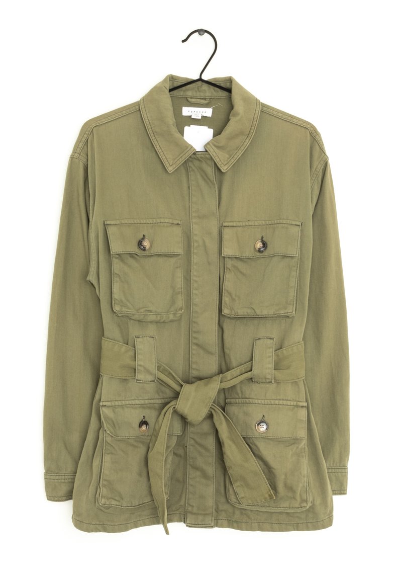 Zielona oliwkowa kurtka z kołnierzem, przednim wiązaniem i dwiema kieszeniami na piersi. Posiada guziki oraz fakturowany materiał.