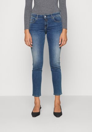 Mėlyni džinsai su siauru siluetu, vidutinio aukščio liemeniu ir lengvu išblukimu. Sukurti su priekinėmis kišenėmis ir dviguba uždarymo sistema.