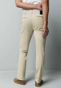 Beige broeken met een slim fit, voorzien van twee achterzakken en een zwart label. Glad textuur en klassiek ontwerp, gecombineerd met bruine schoenen.