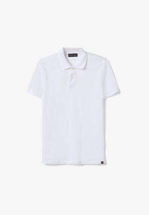 Polo blanc à manches courtes avec col et deux boutons, doté d'une petite étiquette noire sur l'ourlet inférieur et d'une étiquette de marque à l'intérieur du col.