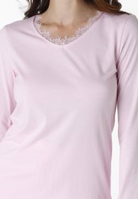 Maglietta a maniche lunghe di un delicato rosa chiaro con scollo a V e dettagli in pizzo sul collo. Realizzata in un tessuto morbido e liscio.