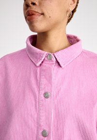 Ružový kordurový košeľa s golierom a striebornými gombíkmi v tvare srdca, so zvislým ribbovaným vzorom a prispôsobeným strihom.