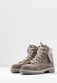 Par de botas de senderismo de ante gris con cordones blancos, cuellos acolchados, ojales de metal y suelas de goma gruesa sobre una superficie blanca.