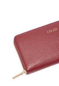 Portafoglio in pelle color vino con superficie testurizzata, cerniera dorata e logo LIU JO in rilievo sul davanti. Forma rettangolare sottile.