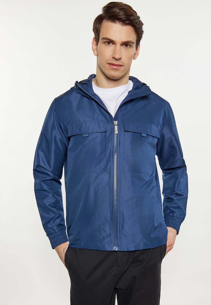 Leichte, blaue Jacke aus glattem Material; verfügt über einen Reißverschluss, zwei Brusttaschen und eine verstellbare Kapuze.