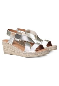Espadrilles à talons compensés en argent métallique avec des brides croisées, détails en jute sur le talon, et une semelle intérieure rembourrée couleur tan. Design à bout ouvert.