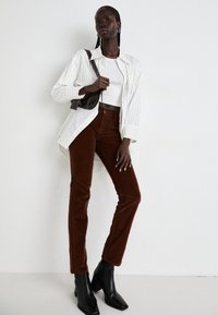 Wit gestreepte button-up shirt, fitted witte crop top, brown corduroy broek en zwarte enkellaarsjes met hak, met een donkere tas en gevlochten haar.