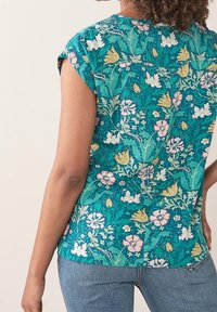 Blomstret bluse i teal med korte ærmer, rund udskæring og en afslappet pasform. Designs inkluderer lyserøde, gule og grønne detaljer.