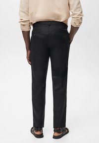 Black dress pants with a slim fit, made of smooth fabric, featuring two back pockets and a mid-rise waist, paired with brown sandals.