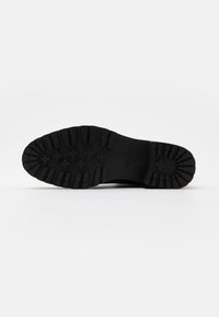 Black rubber sole of a boot featuring deep treads and hexagonal patterns. The underside is flat with branding near the heel.