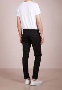 Czarne chinosy o slim fit, z dwoma tylnymi kieszeniami i szlufkami na pasek, w połączeniu z gładką białą koszulką i białymi trampkami.