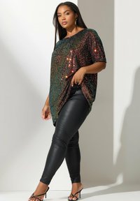 Top de lentejuelas con un degradado de tonos verdes, dorados y rojos, con un ajuste holgado y drapeado lateral; combinado con leggings de cuero negros.