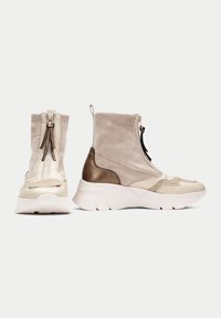 Botas de tobillo de tela sintética beige con cierre de cremallera, acentos en bronce contrastantes y una suela blanca gruesa con detalles texturizados.