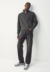 Felpa con zip grigio scuro a maniche lunghe, abbinata a jeans scuri e sneakers grigie. Tessuto liscio, design casual e vestibilità comoda.