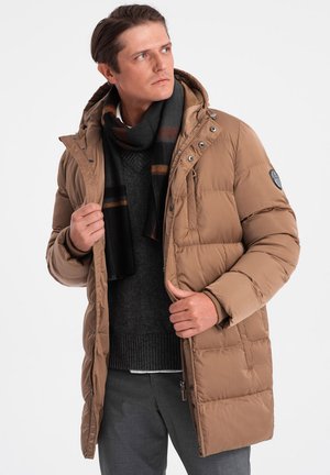 Brun puffjacka med huva, dragkedjestängning och tryckknappar. Bärs över en mörk tröja och svartrandig scarf. Grå byxor som underdel.