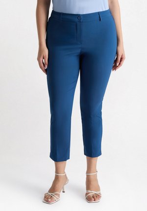 Pantaloni blu a croppato con una texture liscia, chiusura con bottone e taglio dritto. Abbinati a tacchi bianchi con fasce.