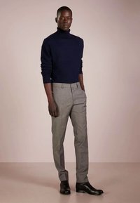 Pulover cu guler înalt bleumarin, pantaloni gri în carouri, conici, și ghete negre de piele până la gleznă. Design simplu cu textură netedă.