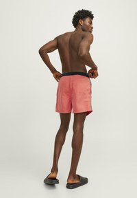 Roze zwembroek met een zwarte elastische tailleband, zijzakken en een achterzak. Lichtgewicht stof met een gladde textuur.